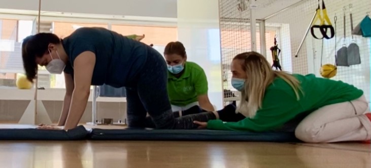 usuario haciendo una práctica en cuadrupedia con la ayuda de dos de nuestras fisioterapeutas.